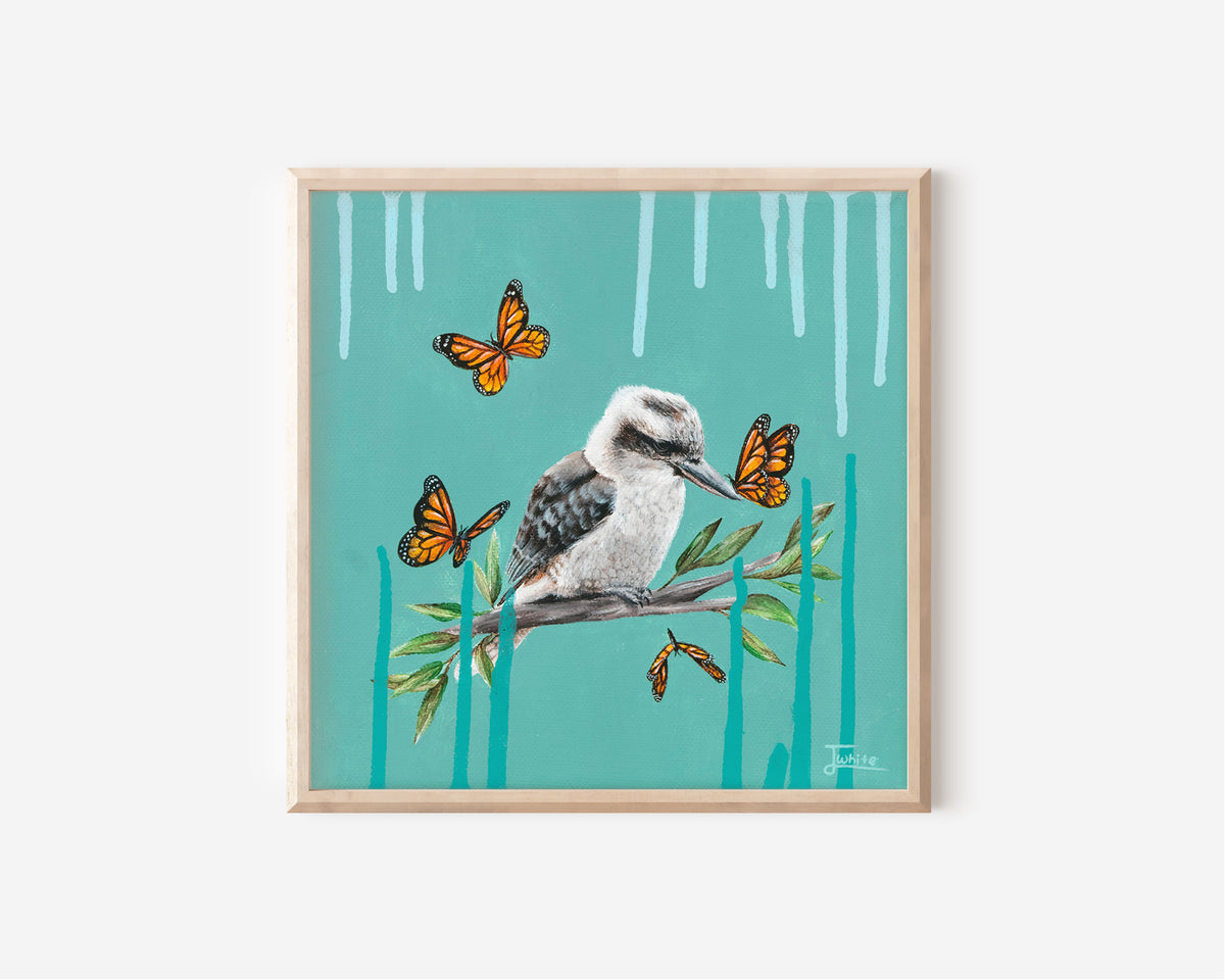 A Fine Art Print hand painted by Australian Artist Jessica Alpert of a peaceful Kookaburra perched on a branch with green leaves against a vibrant turquoise background. Pale blue and deep turquoise paint drips extend from the top and bottom of the canvas. 4 orange monarch butterflies surround the Kookaburra, with one landing on it's beak.