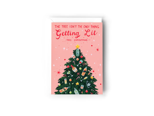 A Christmas greeting card with a pink background, featuring a green Christmas tree decorated with bottles and ornaments, and the text 'THE TREE ISN'T THE ONLY THING Getting Lit THIS CHRISTMAS!' by Australian Artist, Jessica Alpert. The card has a white envelope behind it and sits on a white background.