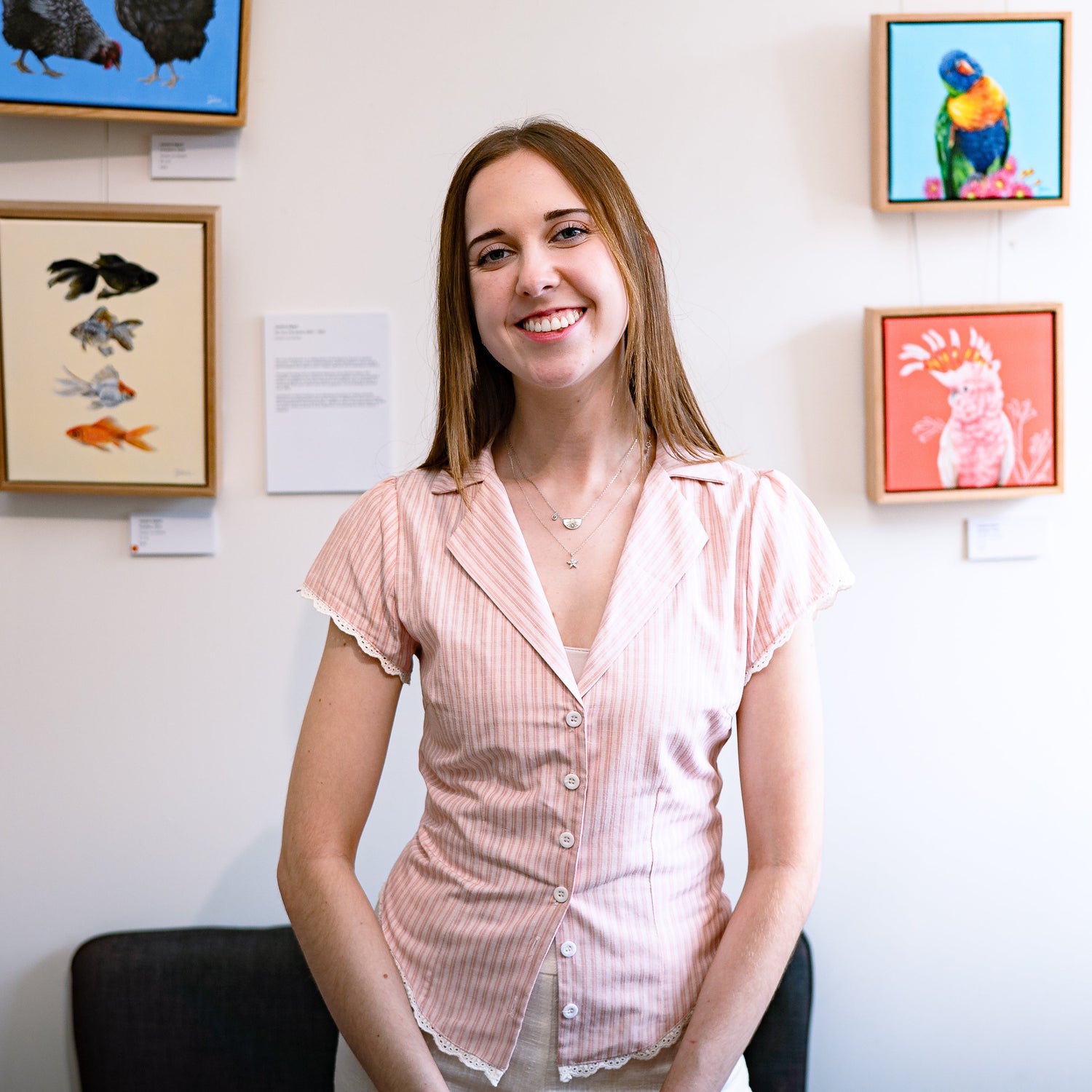 Artist Jessica Alpert standing and smiling in front of her original acrylic paintings at her 'Wild Whimsy' exhibition.