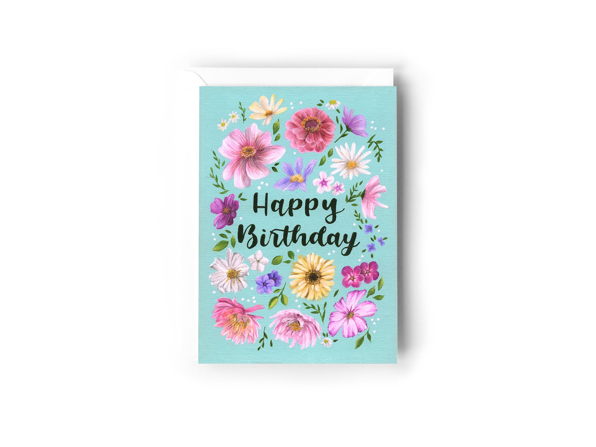 A Birthday Card design hand painted by Australian Artist Jessica Alpert featuring an array of pretty pink, purple, yellow and white flowers and green foliage against a turquoise background. The words 'Happy Birthday' are written in a script font in the centre of the card surrounded by the florals and white dots. The card has a white envelope behind it and sits on a white background.