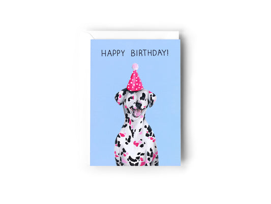 A birthday card design hand painted by Australian Artist Jessica Alpert of a smiling dalmatian dog with black and pink spots wearing a pink polka dot party hat. The card has a blue background and has the words 'Happy Birthday' written at the top.
