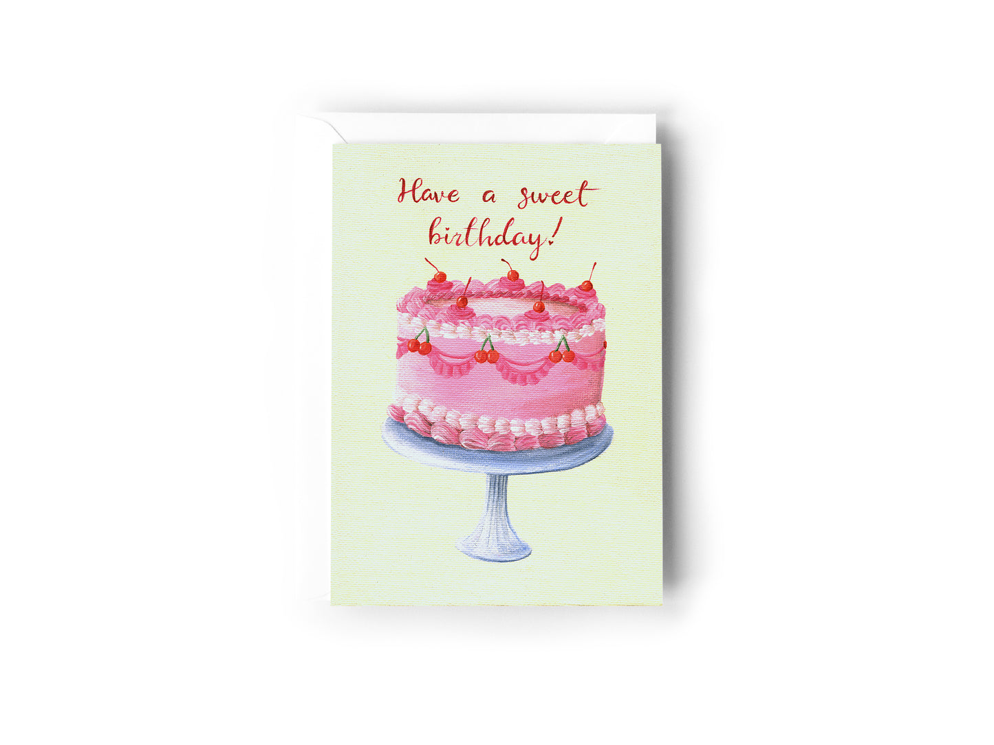 A Birthday Card design hand painted by Australian Artist Jessica Alpert with a pretty pink cake covered n decorative icing and cherries, sitting on top of a silver cake stand on a cream background, with the words 'Have A sweet Birthday!' written in red script above the cake. The card has a white envelope behind it and sits on a white background.