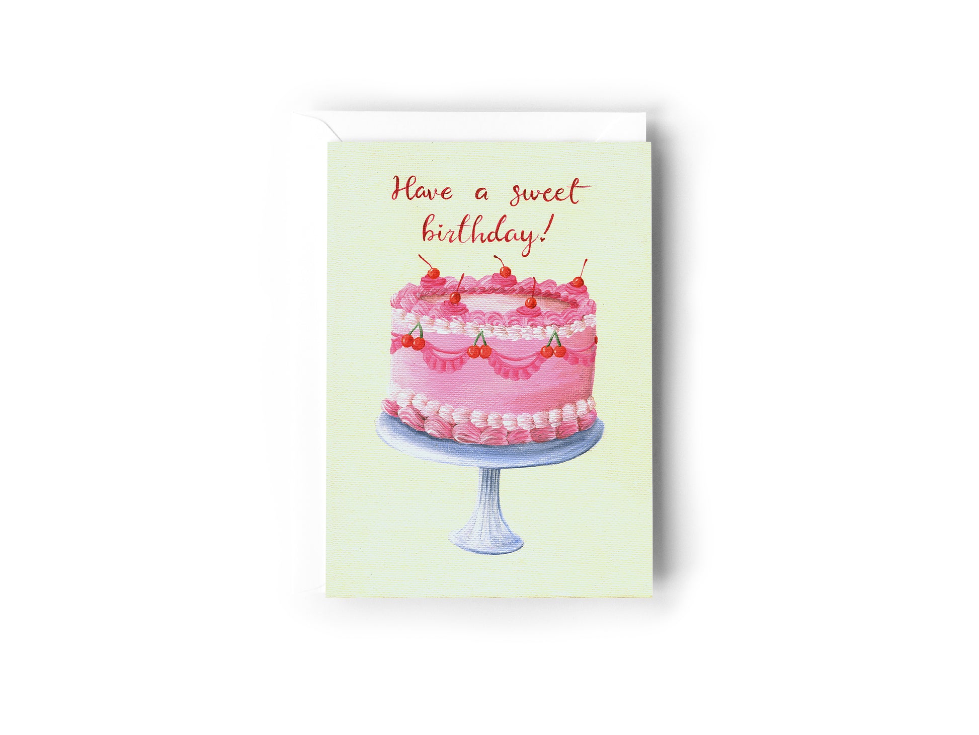 A Birthday Card design hand painted by Australian Artist Jessica Alpert with a pretty pink cake covered n decorative icing and cherries, sitting on top of a silver cake stand on a cream background, with the words 'Have A sweet Birthday!' written in red script above the cake. The card has a white envelope behind it and sits on a white background.