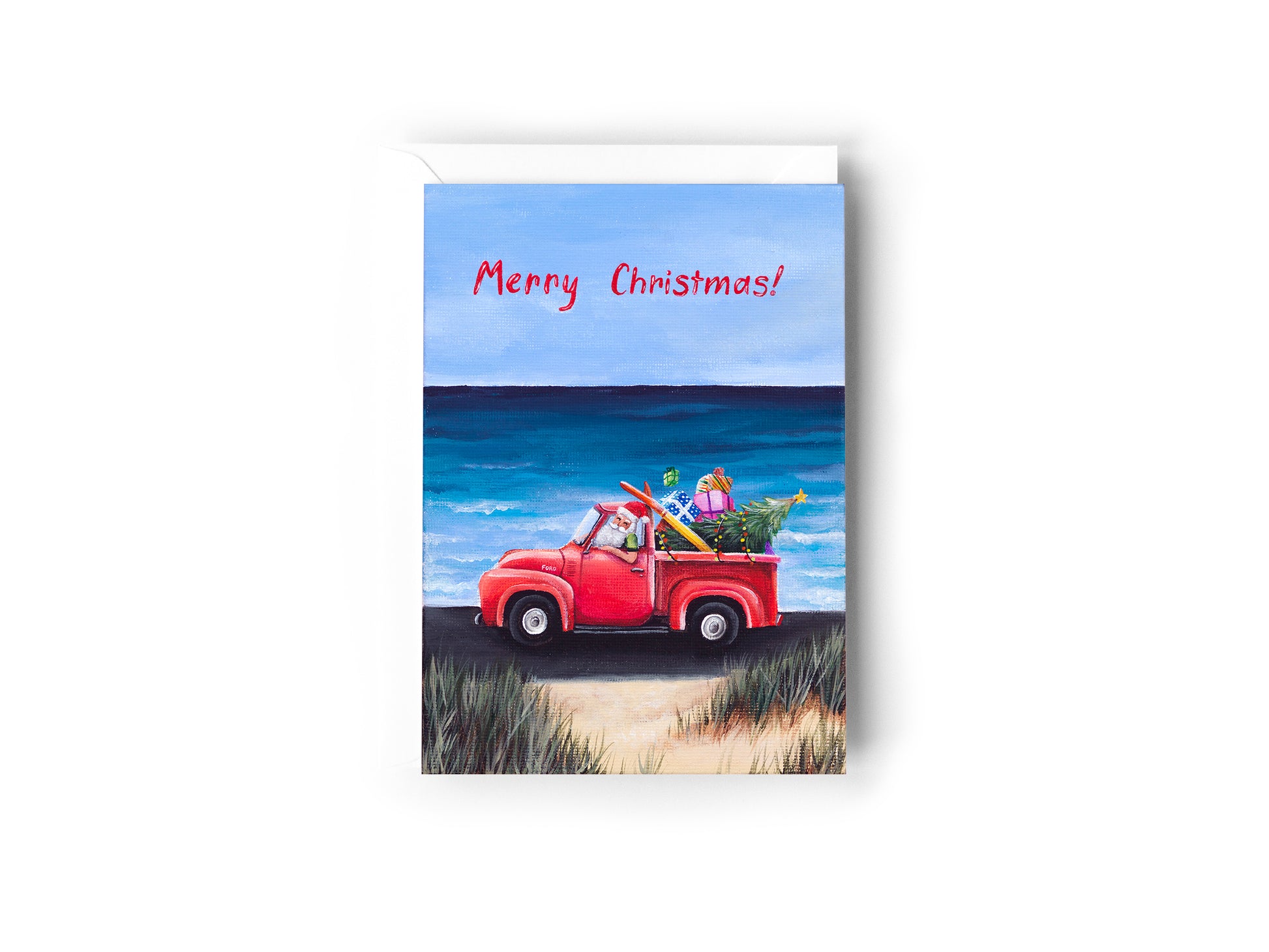 A Christmas card design hand painted by Australian Artist Jessica Alpert, of summer Santa driving a red truck ute on a beachside road, with the ocean and sand surrounding him. The tray of the truck is filled with a Christmas tree, presents and a surfboard. 'Merry Christmas' is written in the skin in red writing. The card has a white envelope behind it and sits on a white background.