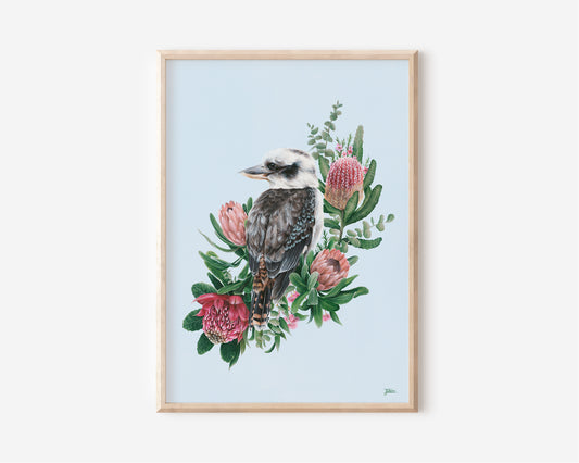 A Fine Art Print hand painted by Australian Artist Jessica Alpert, of an Australian Kookaburra bird looking to his left peacefully, perched amongst pretty green and pink native foliage and flowers, against a soft baby blue background.