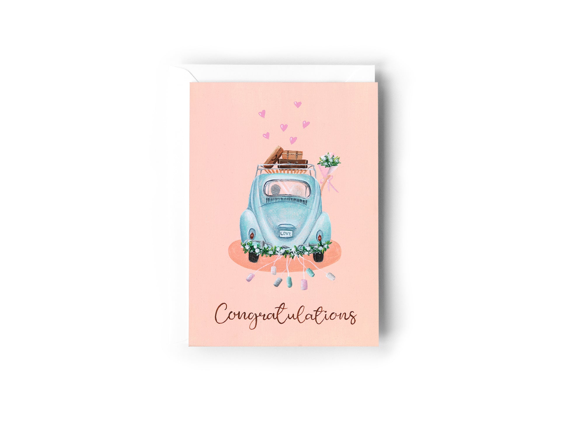 A greeting card design hand painted by Australian Artist Jessica Alpert of a baby blue Volkswagon beetle car driving away, with a bride and groom in the car with the bride holding her bouquet of flowers out the window. Vintage suitcases sit on the roof rack of the car, flowers line the bumper with cans extending off the car. The word 'Congratulations' is written on the bottom of the card in a script font. The card has a white envelope behind it and sits on a white background.