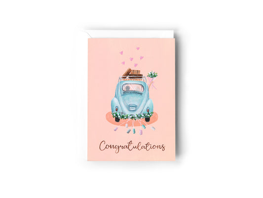 A greeting card design hand painted by Australian Artist Jessica Alpert of a baby blue Volkswagon beetle car driving away, with a bride and groom in the car with the bride holding her bouquet of flowers out the window. Vintage suitcases sit on the roof rack of the car, flowers line the bumper with cans extending off the car. The word 'Congratulations' is written on the bottom of the card in a script font. The card has a white envelope behind it and sits on a white background.
