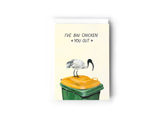 A greeting card design hand painted by Australian Artist Jessica Alpert with a bin chicken on a green and yellow garbage bin illustration entitled 'I've Bin Chicken You Out'. The card has a white envelope behind it and sits on a white background.