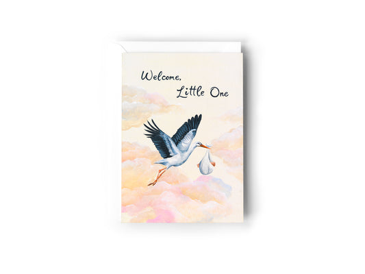 A greeting card design by Australian Artist Jessica Alpert, of a stork bird holding a baby in a blanket from it's beak, flying amongst a pastel coloured sky filled with fluffy clouds. The card has the words 'Welcome Little One' written in a script font at the top of the card. The card has a white envelope behind it and sits on a white background.