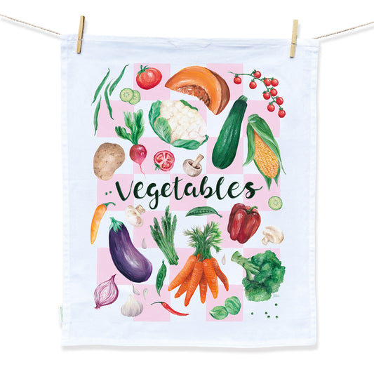 A white tea towel design hand painted by Australian Artist Jessica Alpert. Vibrant, detailed vegetables in a fun collage layout cover the tea towel with a soft pink check patter beneath the vegetables. The word 'Vegetables' is written in a script style in the centre of the tea towel.